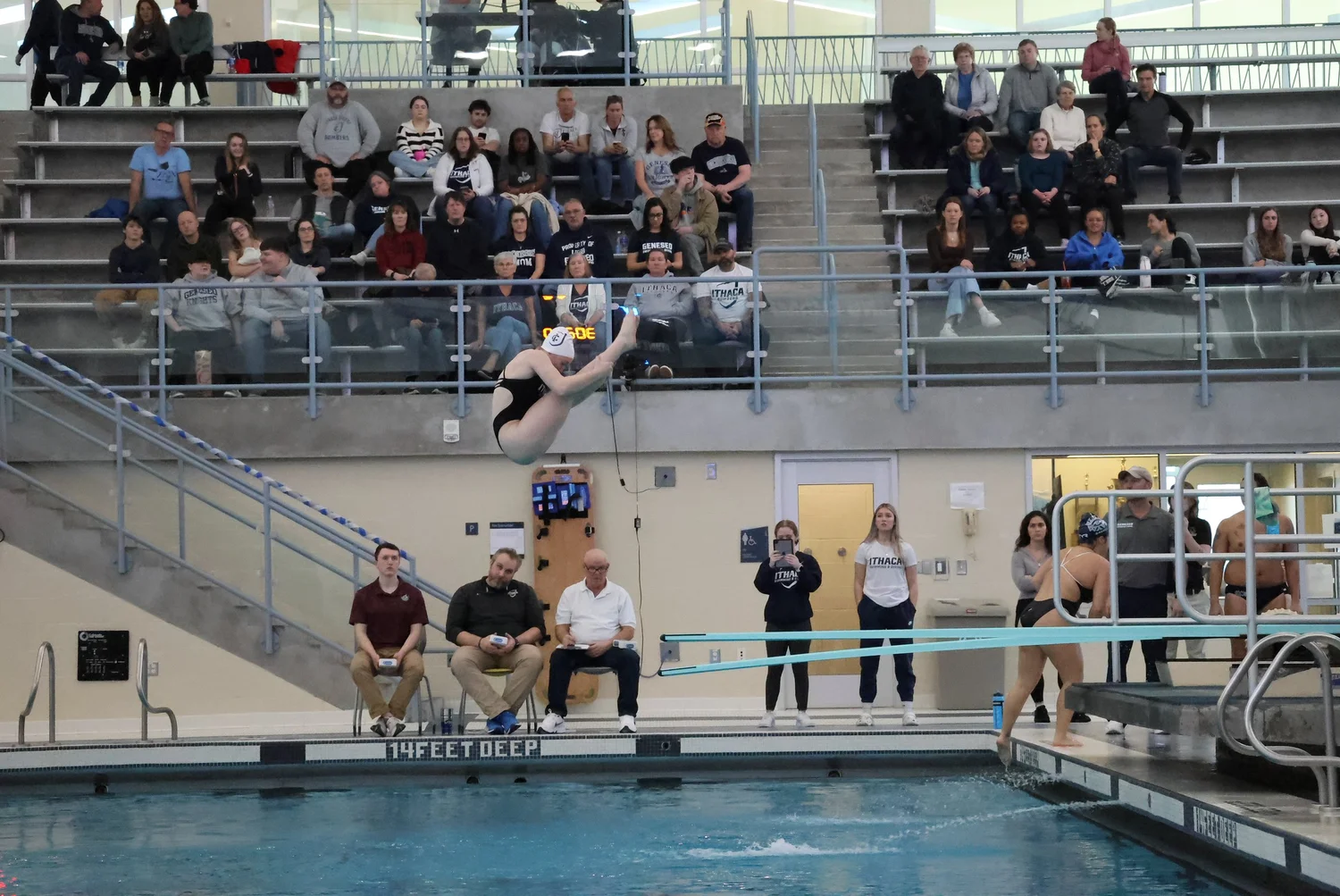 Photo of an Ithaca College diver performing a springboard dive in front of a crowd.